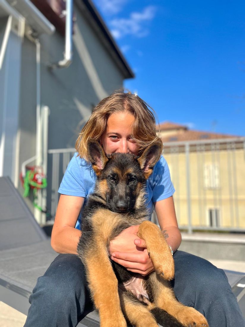 Anna abbraccia Tequila, cucciolo di pastore tedesco, al sole